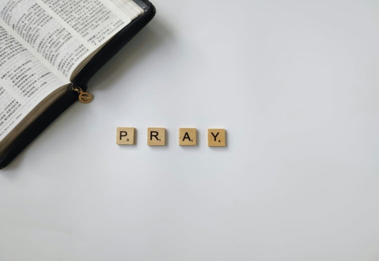 National Day of Prayer is call to pray for the many needs of this nation. The image uses scrabble letters to spell out pray with the corner of a Bible in the background.