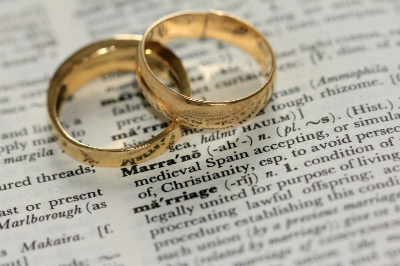 Two golden wedding rings on top of a dictionary with the definition of marriage.