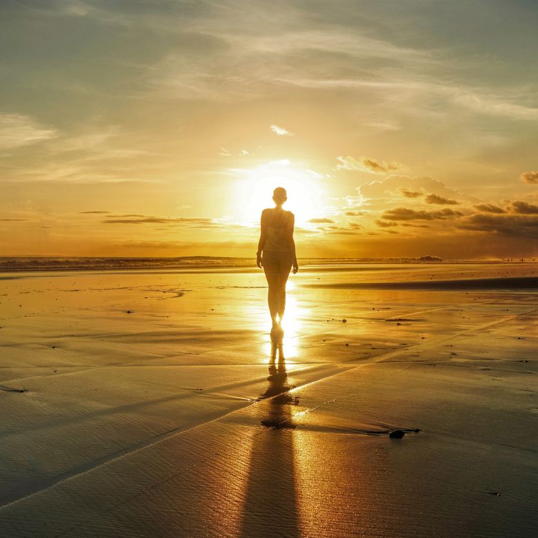 A person walking on the sand and water towards the sun. Waling towards truth