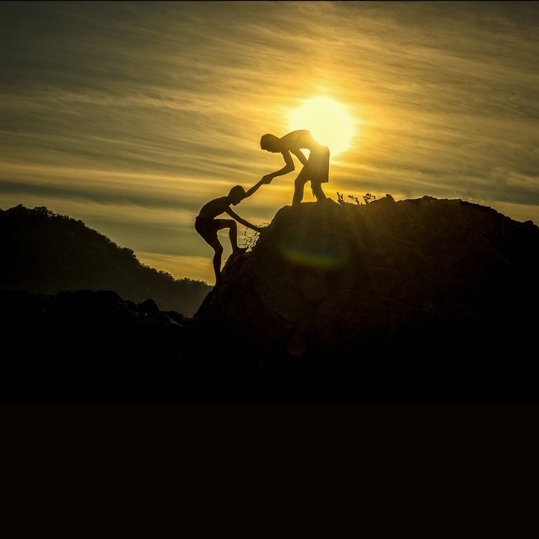 Someone helping another person up a mountain
