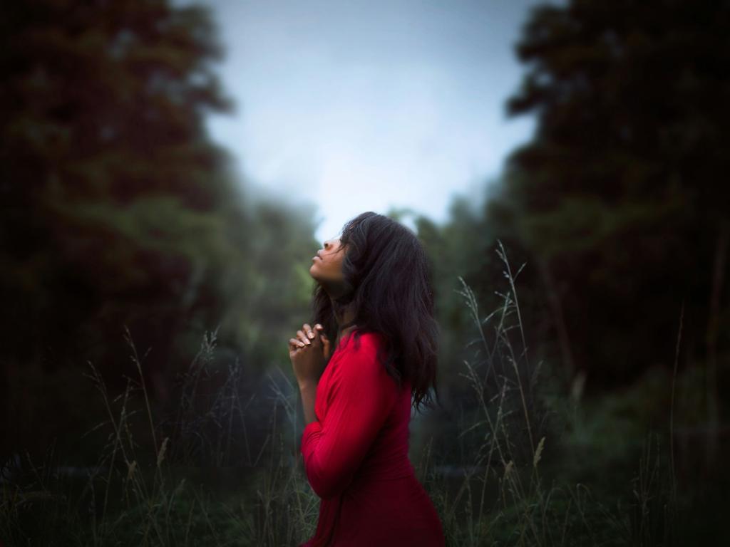 Woman in red shirt standing among trees praying. What does the Bible say about healing prayer?