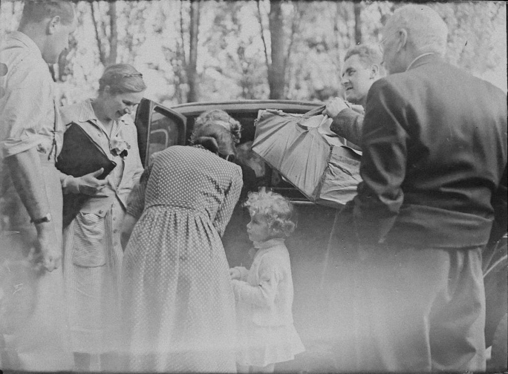 Black and white photo of a family or multiple generations standing in front of a car.