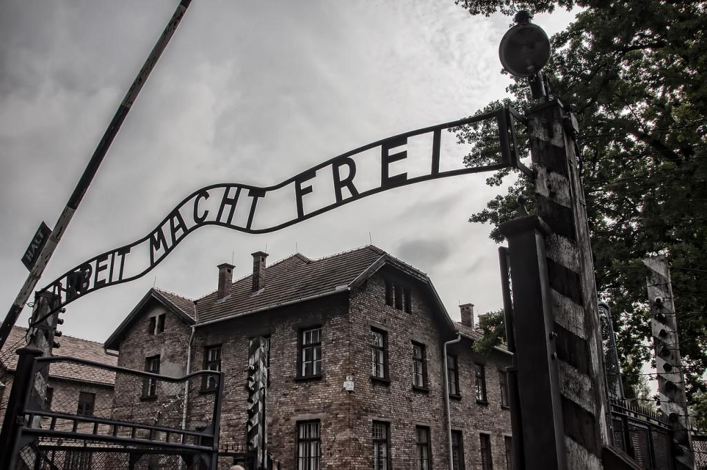 A black and white photo of the Auschwitz sign above the camp entrance that says, Arbeit Macht Frei."