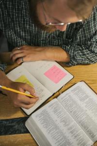 Man studies the Bible with a pencil in his hand, writing in a journal