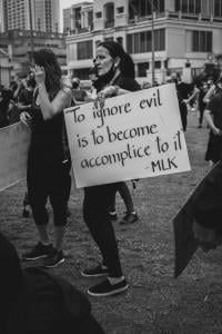 A woman holds a protest sign quoting Martin Luther King Jr.: "To ignore evil is to become accomplice to it"