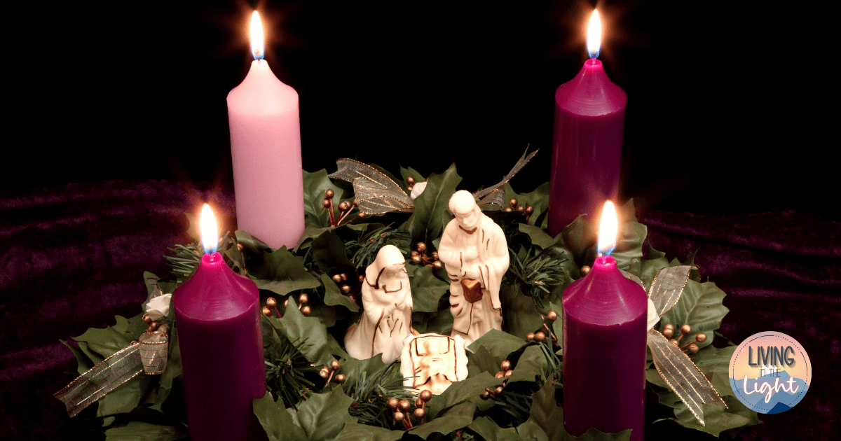 Advent wreath with lit purple and pink candles surrounding a nativity scene.
