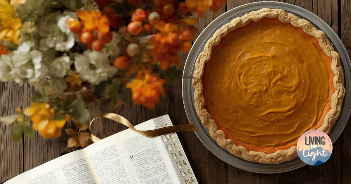 Open Bible beside a pumpkin pie on a rustic wooden table with fall flowers.