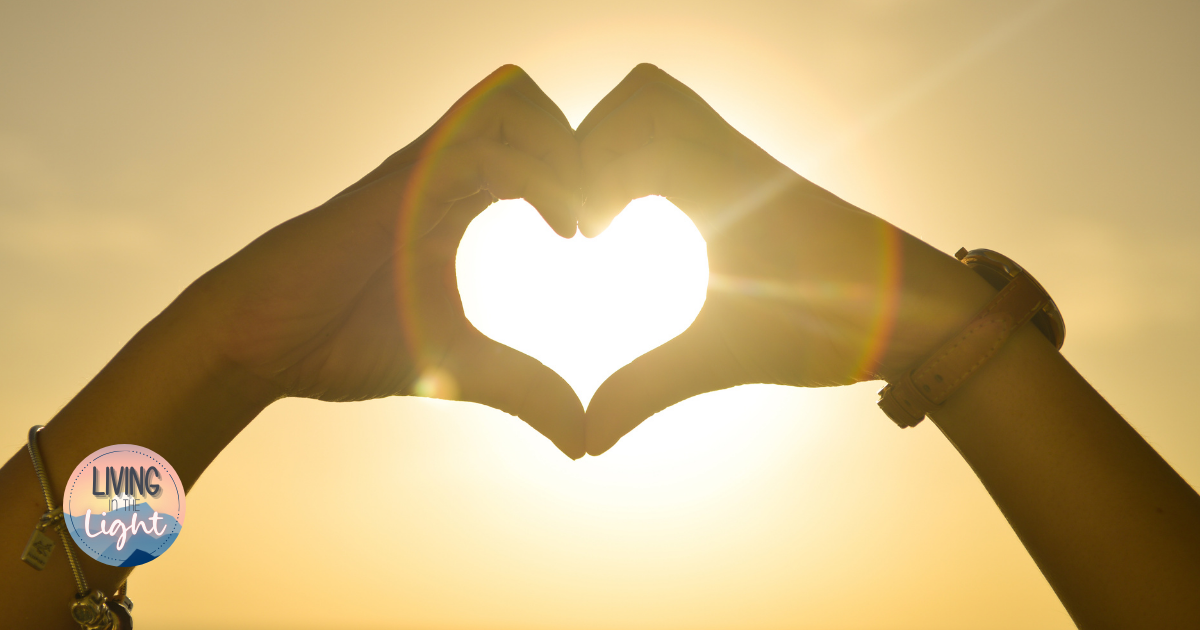 Hands forming a heart shape in front of the sun with warm golden light.