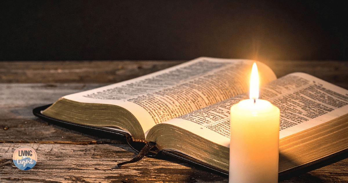 Open Bible on a wooden table beside a lit candle in soft light.