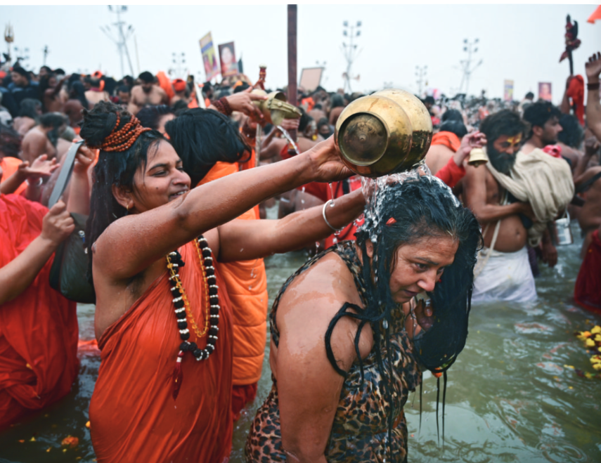 A saffron clad woman pouring sacred water over another woman.