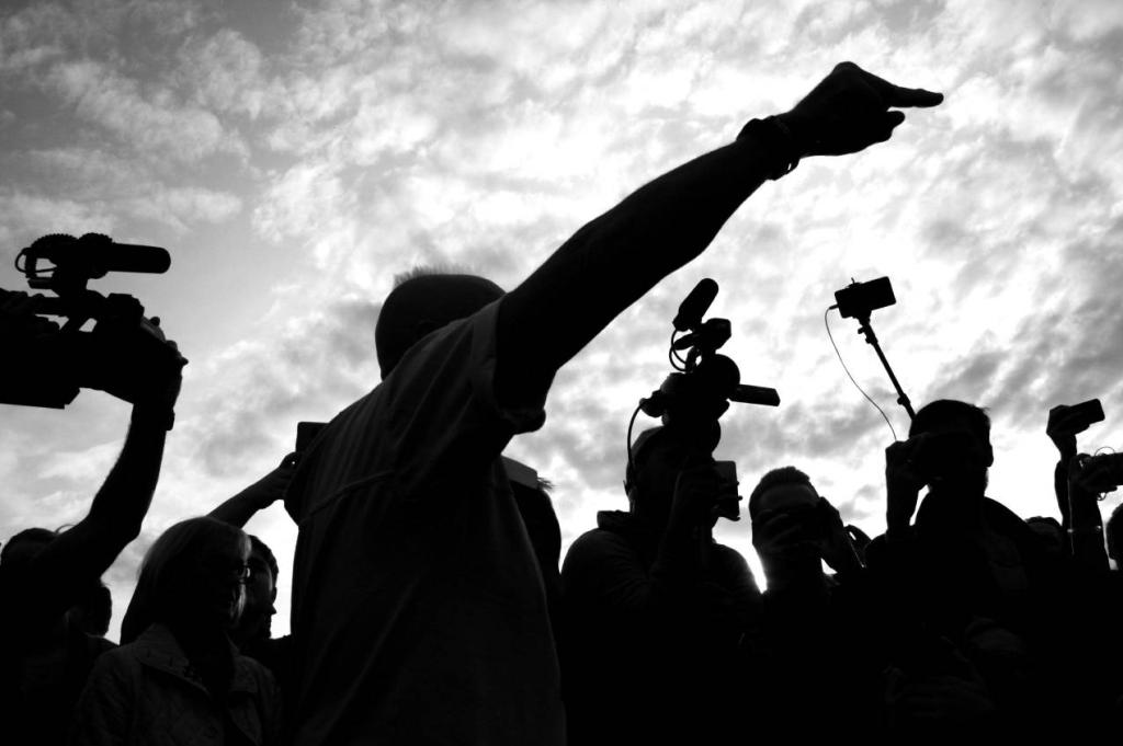 Journalists are silhouetted against the sky.