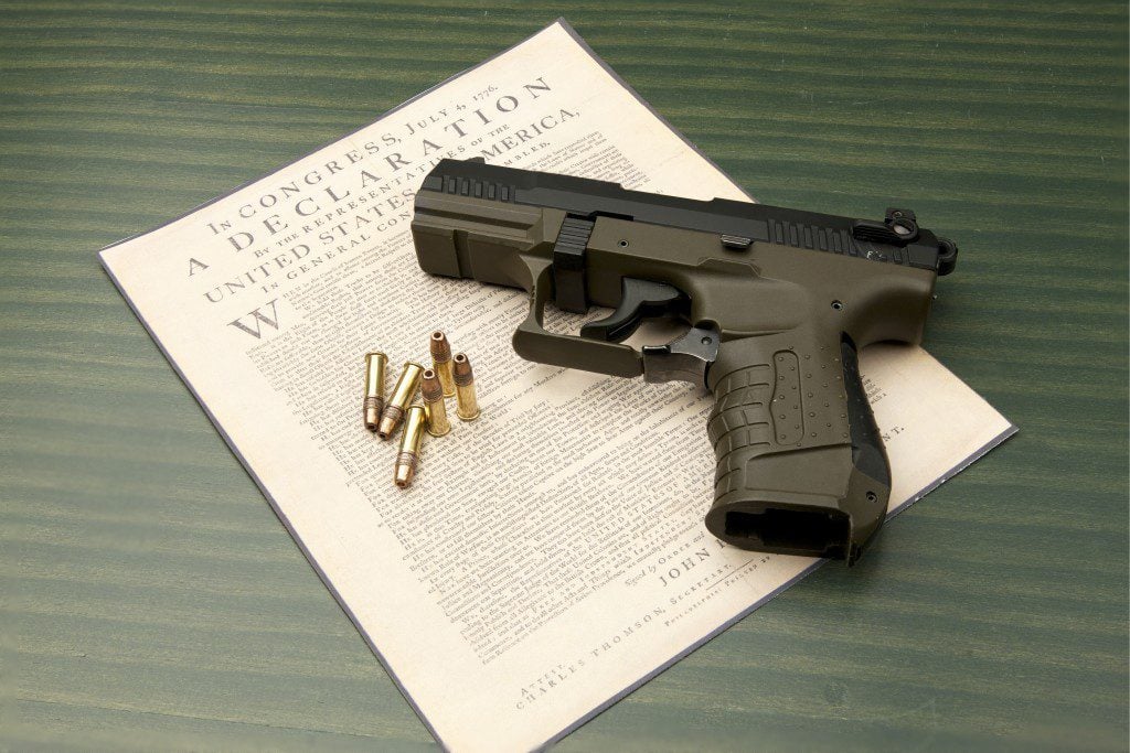 A close up of a hand gun with bullets resting on the Declaration of Independence.