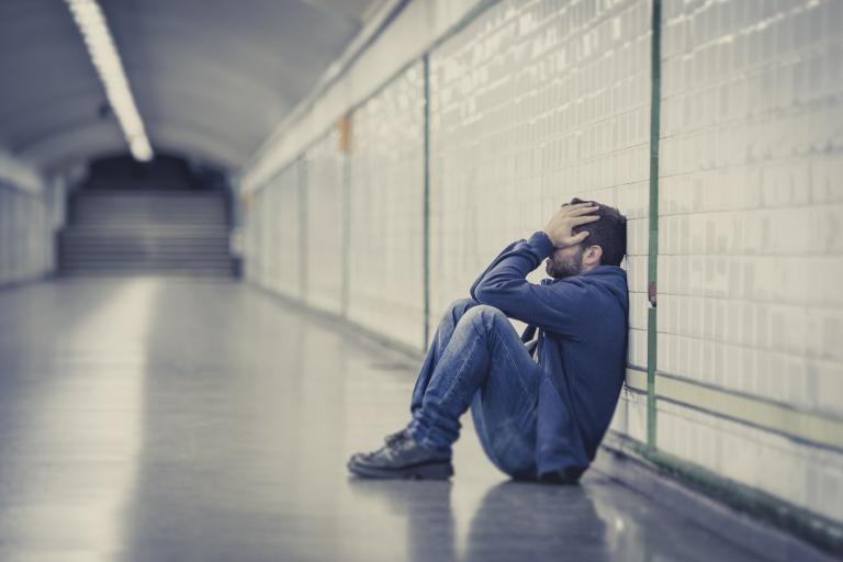 Young man abandoned lost in depression sitting on ground street subway tunnel suffering emotional pain, sadness and looking destroyed and desperate leaning on wall alone
