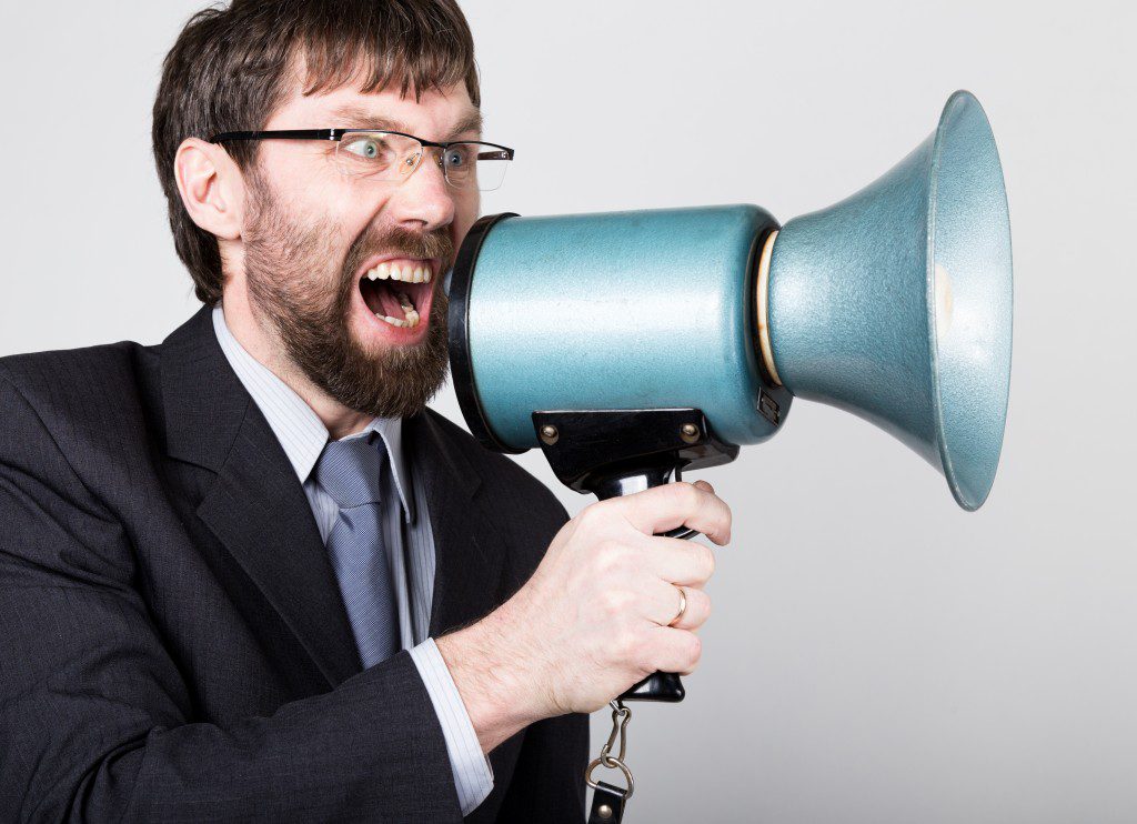 bearded businessman yelling through bullhorn. Public Relations. man expresses various emotions. photos of young businessman wearing a suit and tie.
