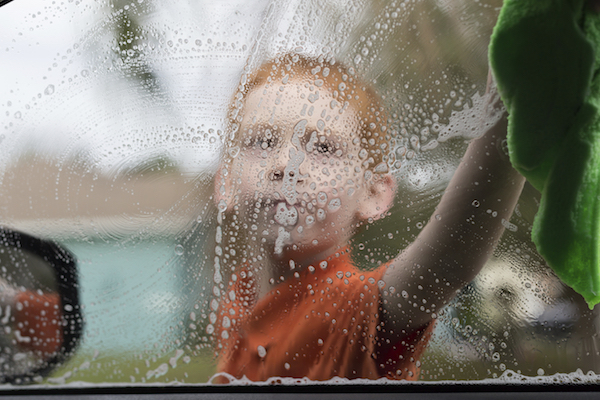 Little boy washing a car window.