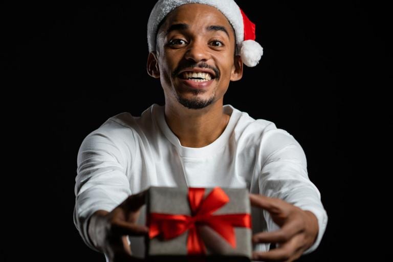 African American man dressed in Santa hat giving a gift