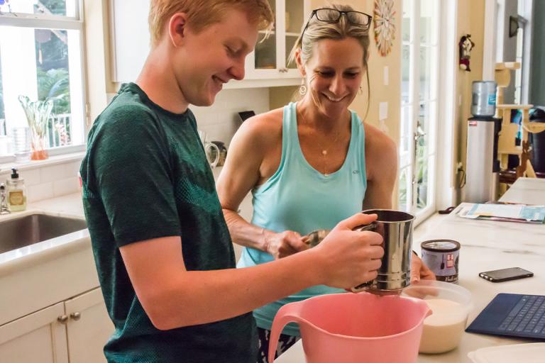 Teen son cooking in kitchen with mom looking on