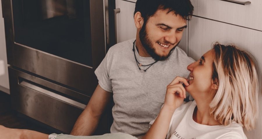 Young couple sits on the kitchen floor embracing and smiling at one another
