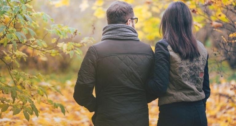 A couple walks arm-in-arm along a leafy path