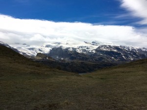 Image: a grassy hill with a snowy glacier and clouds beyond it.