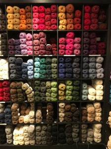 Image: multicolored skeins of yarn on a set of floor-to-ceiling shelves.