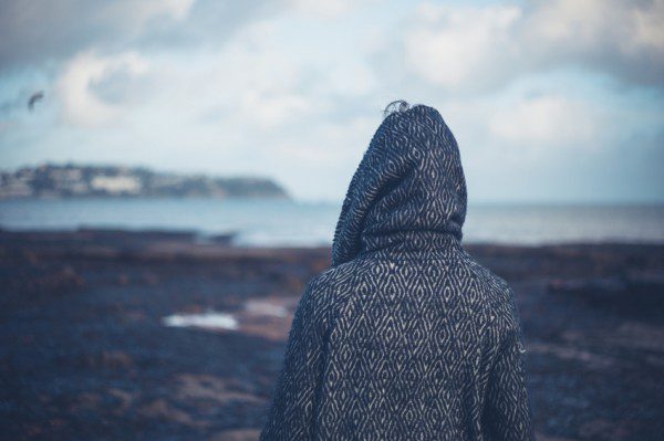 A young woman wearing a hooded coat is walking on a dramatic beach in the winter