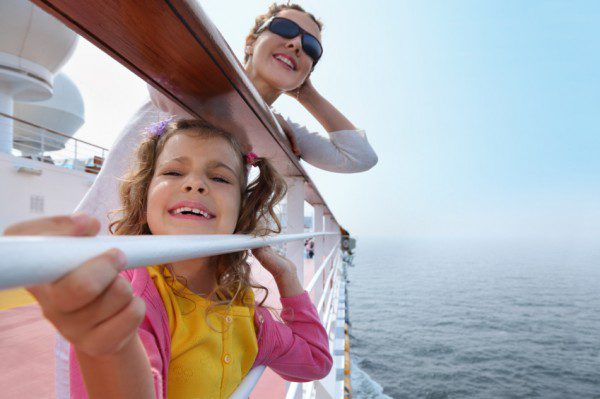 Happy mother and little daughter stand on board of ship and clings to railing