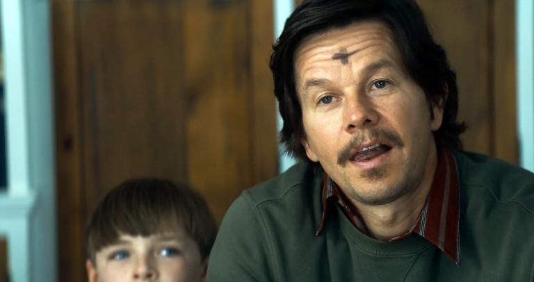 A man with a mustache and an Ash Wednesday cross on his forehead sits next to a boy.