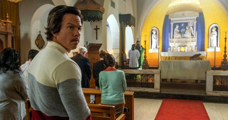 A man standing in a church pew looks back.