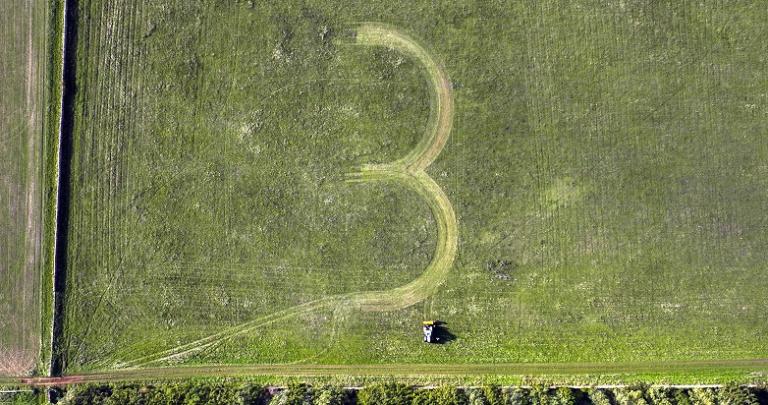 A number 3 is inscribed into a farm field, with a tractor nexte to it.