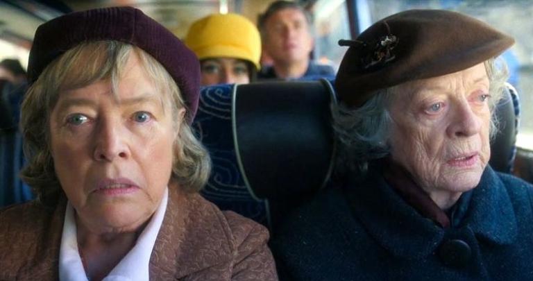Two older women in hats ride on a bus.