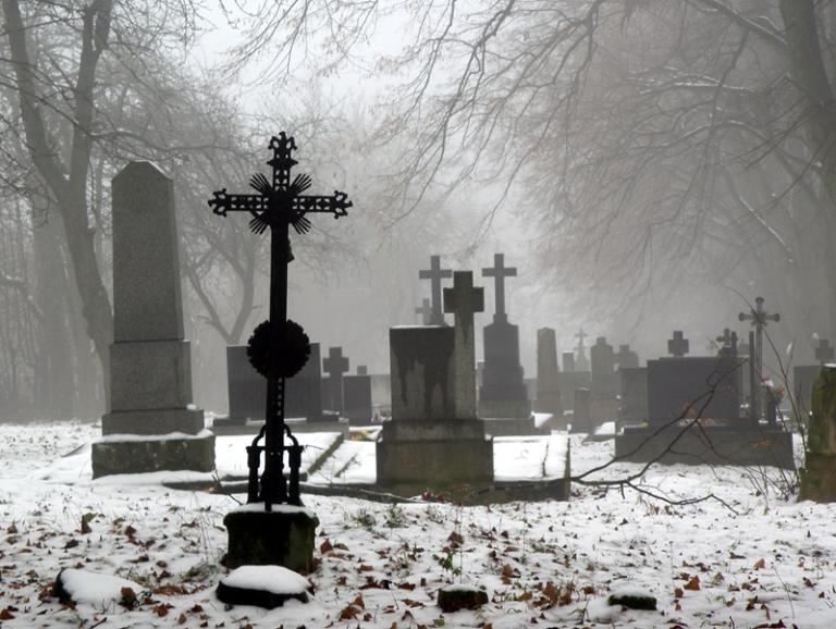 Old Catholic cemetery in winter. There is some snow on the ground and there is fog around.