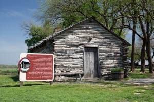 a photo of a small cabin in a field with a red sign in front explaining Laura Ingalls Wilder