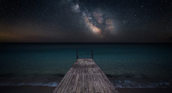 Milky way over che seashore and small wooden jetty in perspective