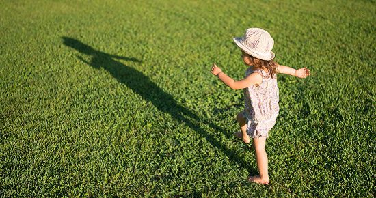 a girl standing on the grass looking at his shadow