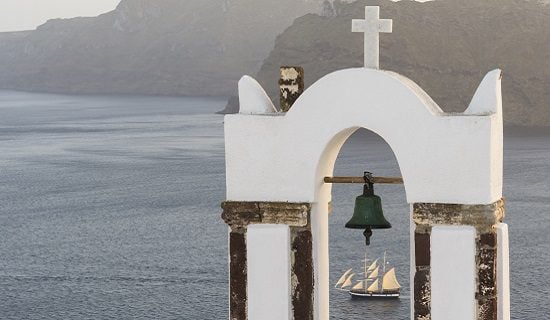 Inside the majesty. Traditional church belfry and sailing boat at sunset in Oia, Santorini, Greece