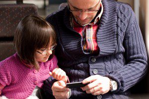 Father and daughter with glasses watching a video on the moile phone while traveling in train