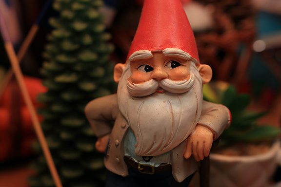 A gnome statue stands relaxed, looking thoughtfully to the side. 