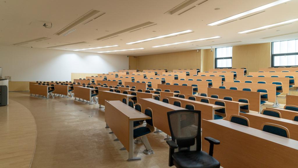 Image of an empty lecture hall filled with chairs and desks.