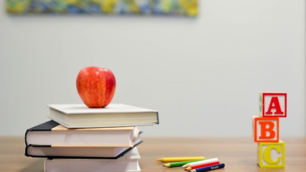 An apple balanced atop books; pencils and blocks with the alphabet letters.