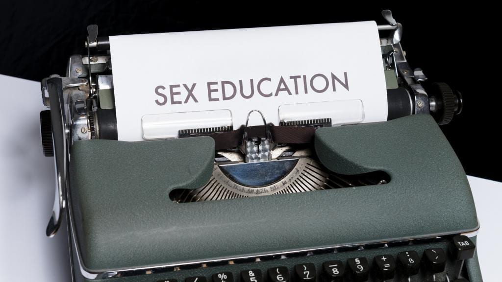 type writer with a piece of paper inserted, on which is printed, sex education