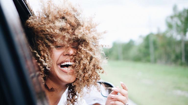 woman with curly hair sticking her head out of a moving car