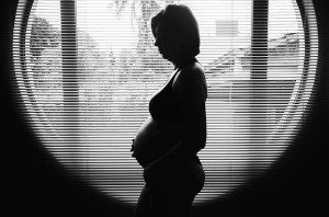 a pregnant woman seen in profile through half-closed blinds