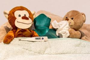 stuffed animals tucked into bed with a tissue, a hot water bottle and a thermometer 