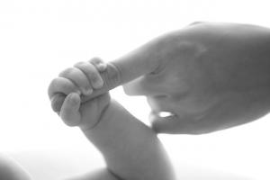 a black and white photo of a newborn baby grasping an adult's finger