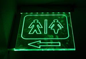 a bathroom sign with stick figures representing "men" and "women." There is an arrow pointing toward the "men" side of the sign