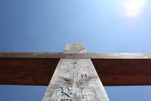 A wooden cross, seen from below, against a bright blue sky