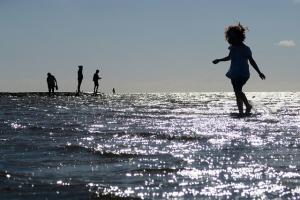 children playing in the shallows in the ocean, silhouetted by a bright sun.