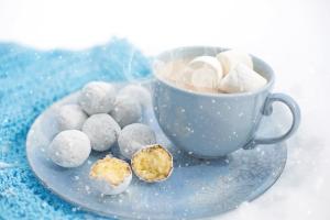 a blue mug of hot chocolate and a plate of doughnut holes on a blue napkin, in the snow