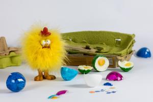 A pompom chicken among broken Easter eggs